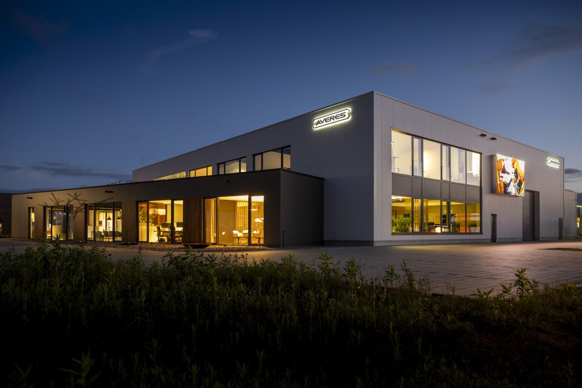Außenansicht der Firmenzentrale der Firma AVERES im dunkel mit Beleuchtung in allen Fenstern und beleuchtetem Logo am Gebäude.